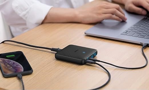 Chargeur multiple USB C posé sur un bureau reliant un smartphone et un pc portable sur lequel une personne travaille dessus.