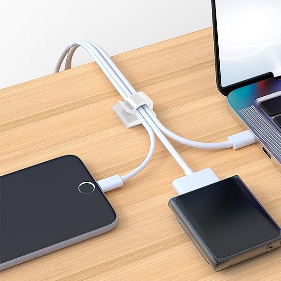 Des clips adhésifs blancs fixent des câbles de charge USB sur un bureau en bois, reliant smartphones et ordinateur portable.